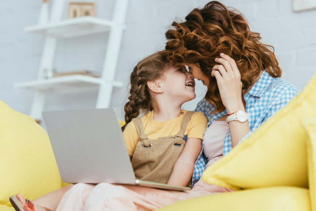 selective focus of happy nanny and child sitting on sofa face to face with laptop